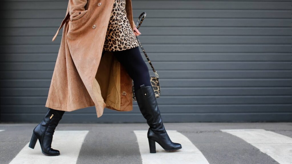 A woman walks on a crosswalk wearing fashionable clothes, demonstrating petite style for autumn. You can only see her legs and torso.
