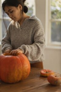 A woman is cutting a pumpkin while wearing a gray big collar blouse