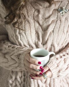 A woman wearing a sweater dress holding a mug of coffee